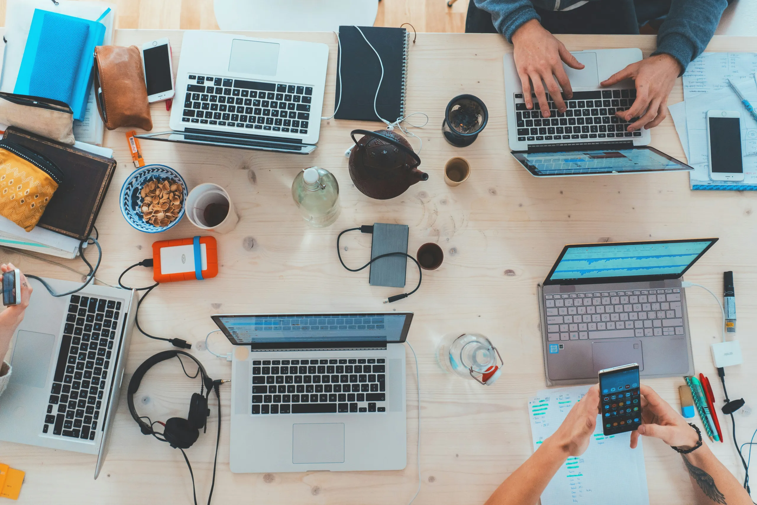 Overhead view of a shared desk where a team works across several laptops, phones and notebooks