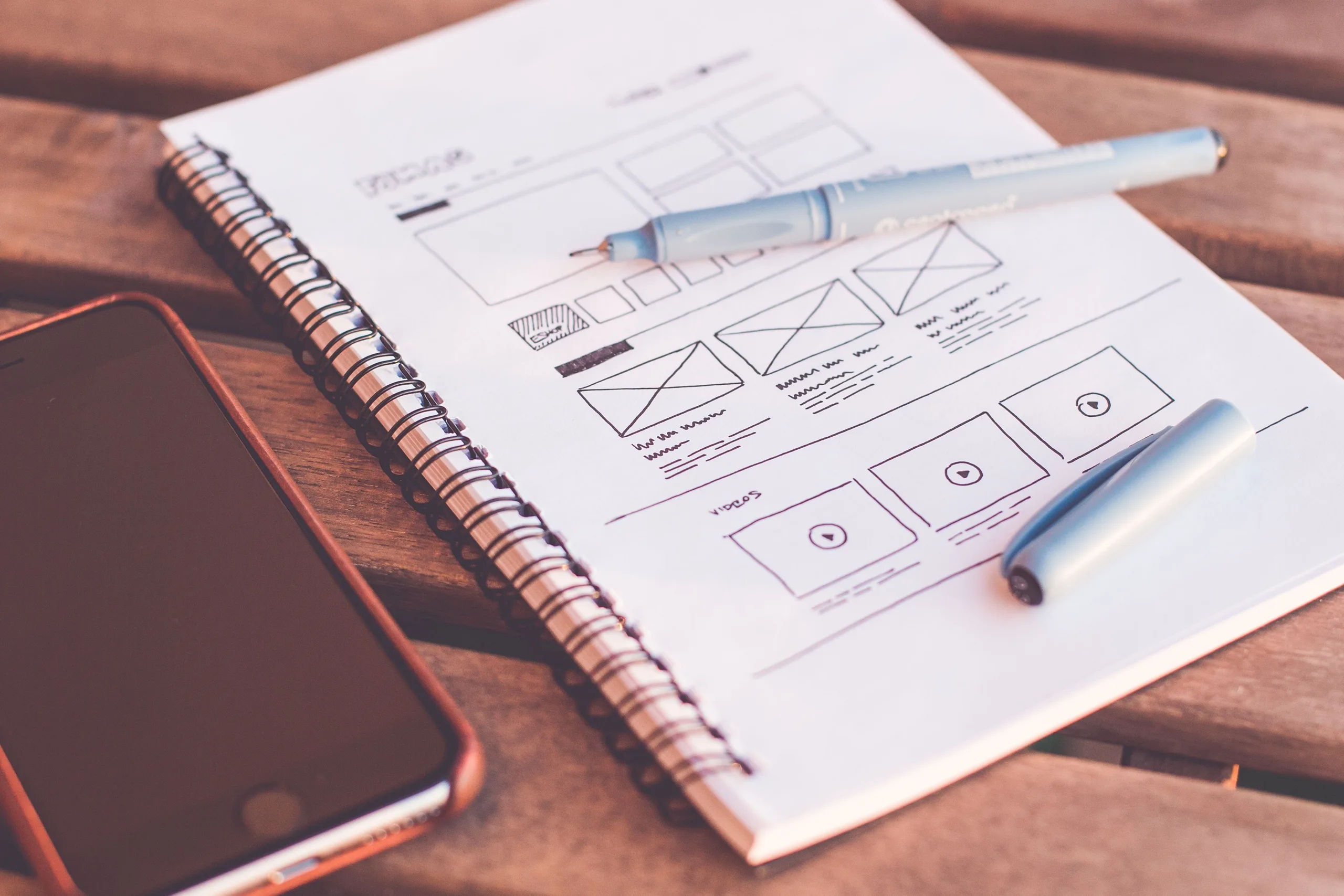 A notebook of hand-drawn website wireframes beside a pen and a phone